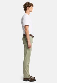 Jasnozielone bawełniane spodnie, dopasowane w fasonie slim fit, prosta nogawka, z bocznymi kieszeniami, w połączeniu z białą bawełnianą koszulką i brązowymi skórzanymi butami.