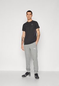 Svart kortermet t-skjorte med logo og grå joggebukser. Buksene har oppbrettede ankler og en hvit logo. Bært med svarte joggesko.