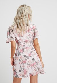 Robe fleurie en rose clair, dotée de manches courtes volantées, d'une taille ajustée et d'un ourlet froncé. Le motif comprend de grandes fleurs roses et blanches.