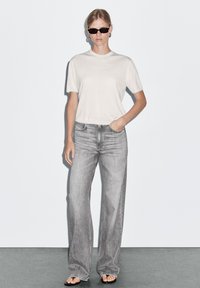 Light gray short-sleeve t-shirt, paired with light gray wide-leg jeans. Black sunglasses, simple hoop earrings, and flat sandals complete the look.
