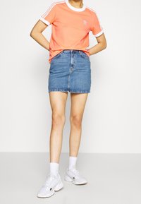 Short-sleeve, bright orange cotton t-shirt with white stripes and round neckline, paired with a denim mini skirt and white sneakers.