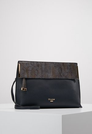 Pochette en cuir noir avec rabat texturé foncé, fermoirs dorés, bracelet, et logo "Dune" sur un socle blanc sur fond uni.