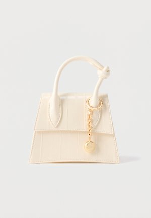 Cream-colored small handbag with a top handle, knot detail, and gold chain charm on a plain light background.