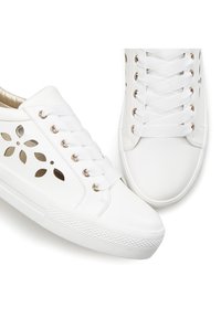 Weiße Sneakers mit perforiertem Blumenmuster, goldenen Akzenten an den Ösen, strukturiertem Gummisohle und flachen weißen Schnürsenkeln. Glattes synthetisches Material.