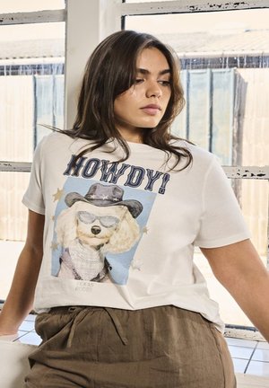 Biała koszulka z grafiką pudla w okularach przeciwsłonecznych i kapeluszu kowbojskim, z napisem "HOWDY!" oraz gwiazdkowymi ozdobami. Luźny krój z krótkimi rękawami.