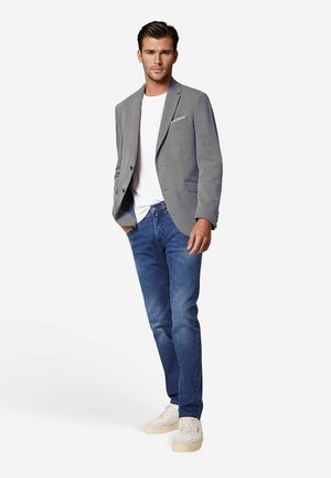 Grijze blazer over een wit T-shirt, gecombineerd met blauwe spijkerbroeken en lichte sneakers. De blazer heeft een enkele zak en een gestructureerde pasvorm.