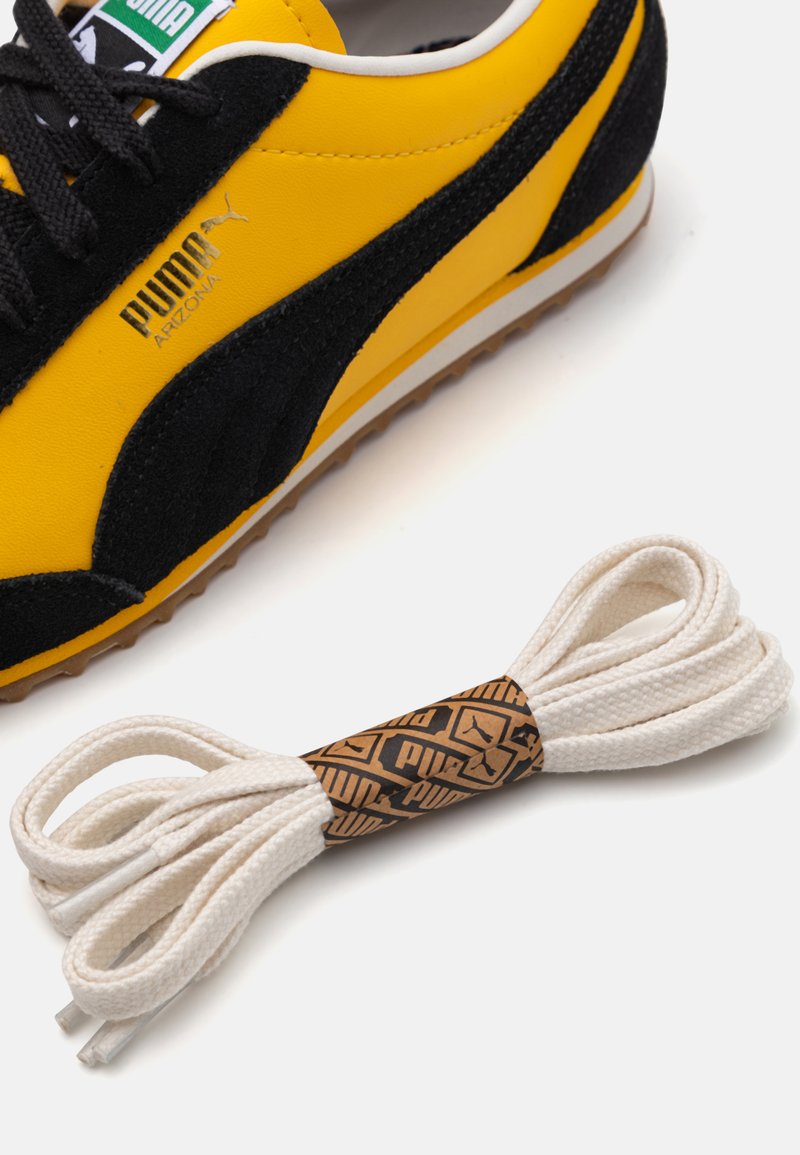 Chaussure de course Puma en cuir suédé jaune vif et noir avec un dessus texturé et une semelle en caoutchouc, accompagnée de lacets en coton blanc avec une étiquette de marque.