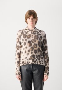 Pull en tricot avec un motif léopard beige, marron et noir, doté d'une taille côtelée et d'un col haut. Porté avec un pantalon en cuir noir.