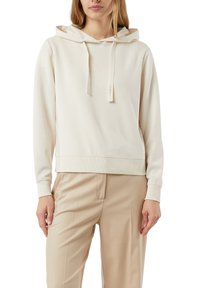 Beżowa bluza z kapturem na troczki, miękka w dotyku, z prążkowanymi mankietami i dolnym wykończeniem. W połączeniu z jasnobeżowymi spodniami tworzy monochromatyczny wygląd.