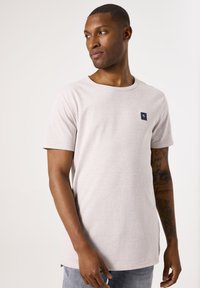 Lichtgrijze katoenen t-shirt met een ronde hals en korte mouwen. Heeft een klein marineblauw logo op de linkerborst en een textuur met een gestreept patroon.