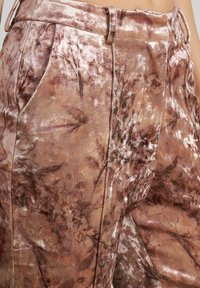 Sam softrosafarbenen Samthosen mit floralem Muster, gefaltetem Vorderteil und seitlichen Taschen für funktionale Details.