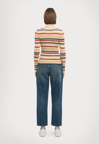 Gestreepte lange mouwen top in geel, rood, zwart en oranje, gecombineerd met hooggetailleerde blauwe spijkerbroek en witte sneakers.