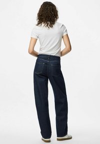 Tumši zilas augstās jostas bikses ar platām kājām, kurām ir divas aizmugures kabatas un gluda tekstūra, apvienotas ar baltu īsām piedurknēm kreklu.