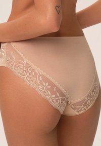 Beżowe majtki z wysokim stanem, wykończone koronką po bokach, z kwiatowymi wzorami i przezroczystymi wstawkami, które dodają tekstury i detali.