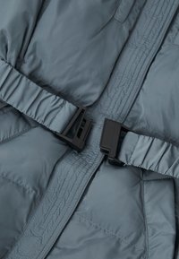 Sivi pufasti jakna od tkanine s glatkom teksturom, s crnim plastičnim kopčama i šivenim detaljima. Dizajn je minimalistički i funkcionalan.