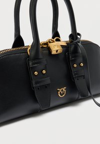 Μαύρη δερμάτινη γυναικεία τσάντα με χρυσά μεταλλικά στοιχεία, διαθέτει φερμουάρ, δύο κοντές λαβές και διακοσμητικό κλείδωμα με σχέδιο έμβλημα.