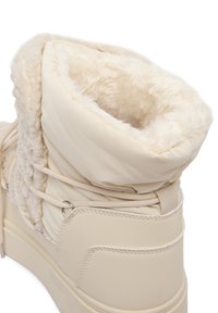 Botă de iarnă bej cu căptușeală groasă din fleece, interior umplut și sistem de prindere cu șireturi, proiectată pentru căldură și confort.