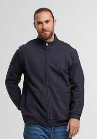 Dunkelblaues Zip-Hoodie mit hohem Kragen, aus weichem Stoff gefertigt. Verfügt über seitliche Taschen und ein kleines Logo in der Nähe des Reißverschlusses.