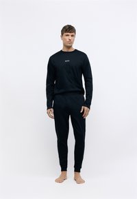 Top negro de manga larga con logo "BOSS", joggers negros a juego, confeccionados con tejido suave y puños acanalados, silueta ajustada, pies descalzos.