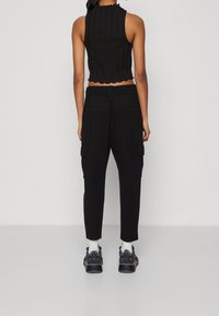 Svart ribbad crop-top med en vågig nederkant, matchad med löst sittande svarta cargo-byxor med sidfickor och elastisk midja.