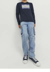 Navy long-sleeve shirt with white and purple "JACK & JONES" logo, paired with light blue cargo jeans and navy sneakers with white laces.