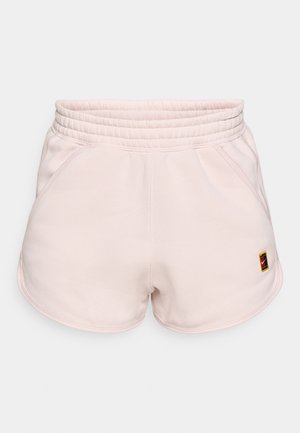Pantalones cortos deportivos de color rosa claro con una banda elástica ancha en la cintura, bolsillos laterales y un pequeño parche con logo en la parte inferior izquierda. Textura de tela suave.