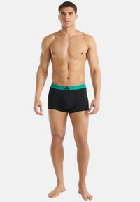 Boxers noirs avec une ceinture élastique verte ornée d'un logo. Le tissu semble lisse et extensible, conçu pour le confort.