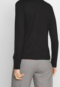 Svart långärmad topp med en slät yta, slim fit och en mittsömskonstruktion på baksidan. Matchad med svart och vit rutiga byxor.