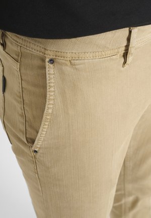 Pantaloni in cotone beige con tasche laterali visibili, tessuto texturizzato e dettagli in metallo. I particolari delle cuciture sono evidenti lungo i bordi.