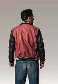 Veste bomber en cuir rouge et noir avec col et poignets côtelés, dotée d'une écusson logo sur la manche et d'un ourlet élastiqué.