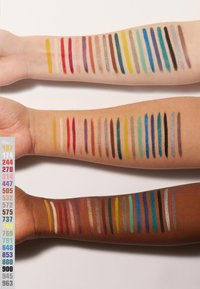 Drie armen tonen kleurrijke cosmetische swatches in verschillende lengtes. De tinten omvatten geel, rood, blauw en metallic, tegen zowel lichte als donkere huidtinten.