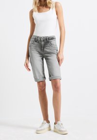 Bermudas de mezclilla gris con dobladillos enrollados, con bolsillos frontales y cierre de botón, combinadas con una camiseta ajustada blanca y zapatillas blancas.