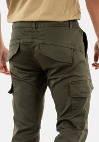 Pantalons cargo vert olive avec une coupe slim, dotés de deux poches arrière et de poches cargo latérales, fabriqués en tissu mélangé coton durable.