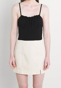 Černý zkrácený top s nařaseným výstřihem a tenkými ramínky, v kombinaci s béžovou mini sukní s předním rozparkem. Hladká tkanina, přiléhavý design.