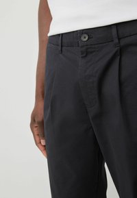 Pantalons navy en tissu lisse, dotés d'une fermeture à bouton, de poches latérales et de plis marqués pour un look sur mesure.