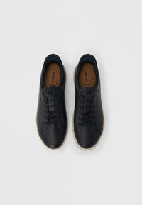 Paire de baskets décontractées en cuir noir avec lacets noirs et semelles beige, vues de dessus sur fond blanc.