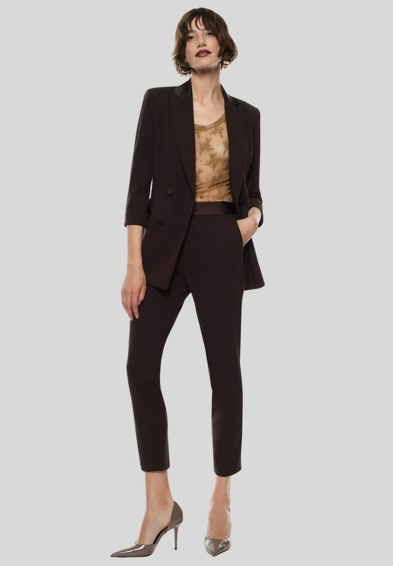 Blazer marrone su misura con design a single-breasted, abbinato a un top con motivo dorato e pantaloni tapered coordinati. Tacchi alti argentati.