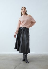 Pink ribbed sweater with off-shoulder design, paired with a black pleated midi skirt and knee-high black boots. Minimalist setting.