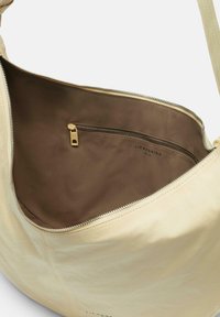 Beige Leder Schultertasche mit einem geräumigen braunen Innenfutter aus Stoff, ausgestattet mit einer Reißverschlusstasche und metallischen Reißverschlussdetails.