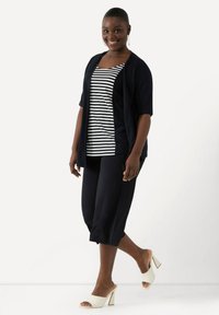 Marinblå cardigan över en randig linne, ihop med beskurna byxor. Vita blockklackade sandaler. Slät tyg med avslappnad passform.