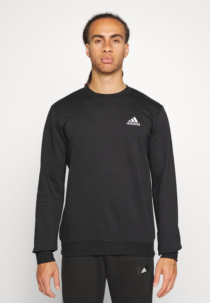 Felpa nera a maniche lunghe in cotone con colletto a girocollo. Presenta un logo Adidas bianco sul lato sinistro del petto e polsini a coste.