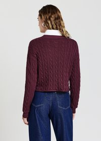 Maglione a collo rotondo in maglia a treccia bordeaux con design cropped e polsini a coste. Abbinato a jeans in denim a vita alta.
