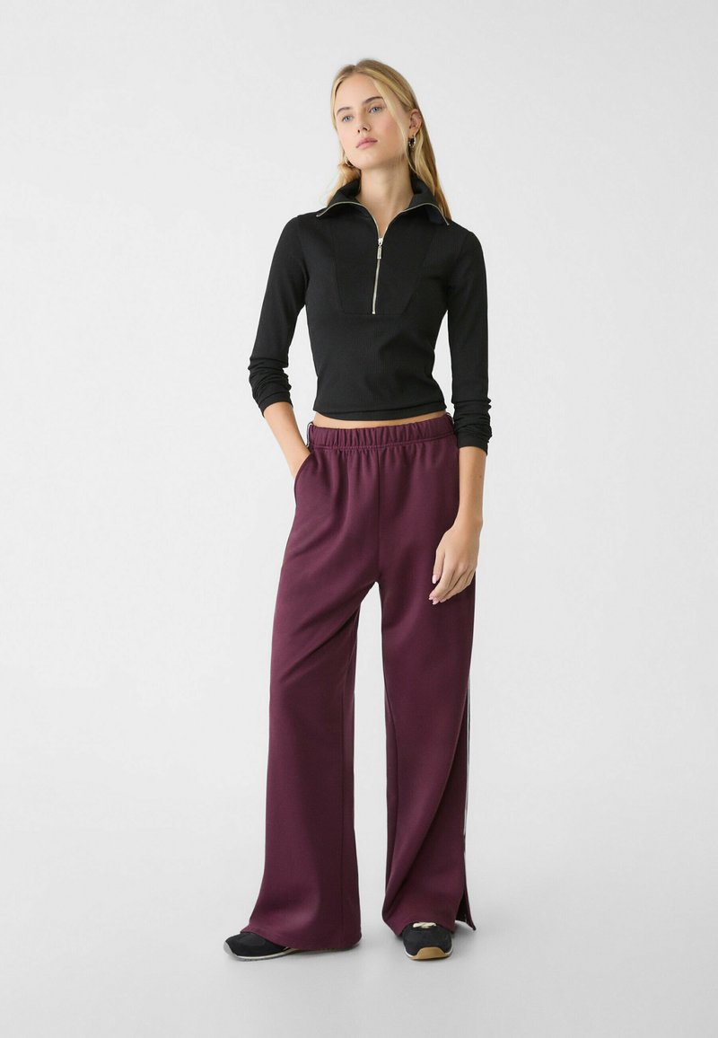 Top a maniche lunghe nera con zip abbinato a pantaloni larghi borgogna a vestibilità comoda. Tessuto morbido e liscio con vita elastica e tasche laterali.