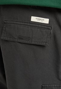 Zwarte stoffen shorts met een gestructureerde weving, voorzien van een achterzak en een wit label met de tekst "ELEMENT CO. SINCE 1992."