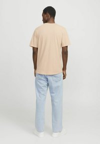 Light beige short-sleeve t-shirt with a round neckline, paired with light blue loose-fit jeans and white sneakers. Basic, casual design.