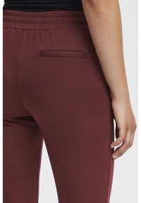 Burgundy sweatpants med resårmidja, som har en platt bakficka och en mjuk tygstruktur.