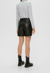 Schwarze Leder-Shorts mit taillierter Passform, die über eine glatte Textur, einen Bund und zwei Gesäßtaschen verfügen. Getragen mit einem hellgrauen Langarmoberteil.