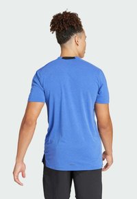 Blauwe korte mouwen T-shirt van zacht materiaal. Voorzien van een gebogen zoom, zijsplitten en een klein logo op de achterkant. Effen ontwerp zonder patronen.