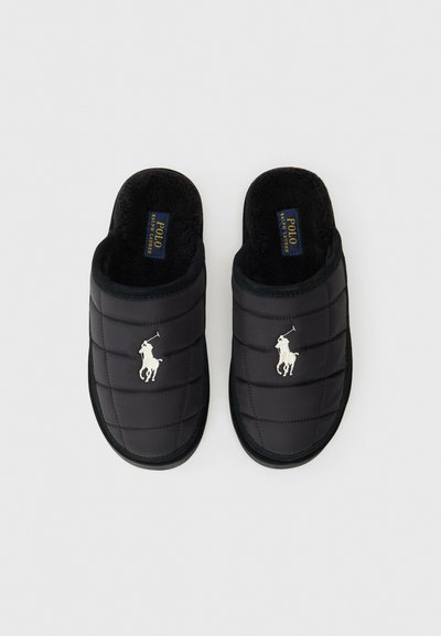 Zwarte gewatteerde instapslippers met een gestructureerd oppervlak, voorzien van een wit logo en een zachte vachtvoering voor comfort. Rubberen zolen voor duurzaamheid.