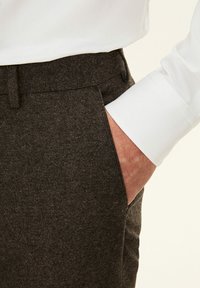 Pantaloni marroni con trama, dal taglio slim, con tasche laterali e frontale piatto, abbinati a una camicia bianca a maniche lunghe.